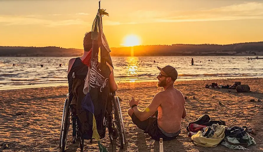 duas pessoas, uma com cadeira de rodas, a ver o por do sol no festival boom